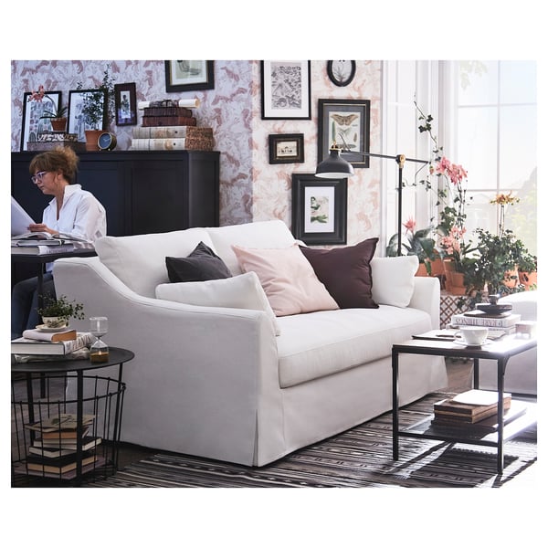 Bright living room with white GURLI sofa, colourful pillows, black side tables, plants, books, and patterned wallpaper.
