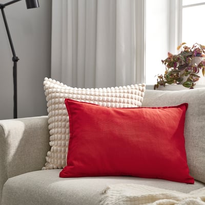 Grey sofa with bright red & white pillows, red larger, textured white, plant on armrest.
