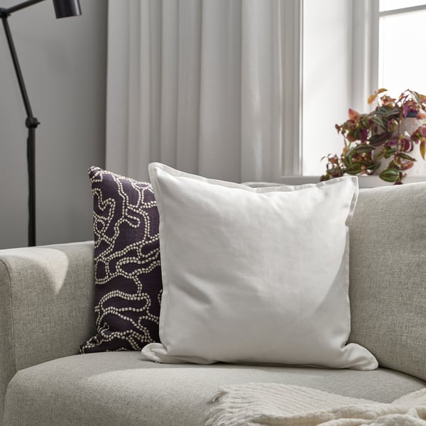 A white cotton cushion on a grey sofa beside a patterned cushion and plant.