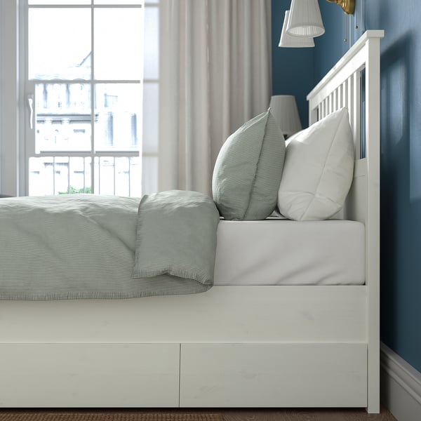 Bed with drawers for storage under side. White, blue bedding, and curtains. Window with city view.