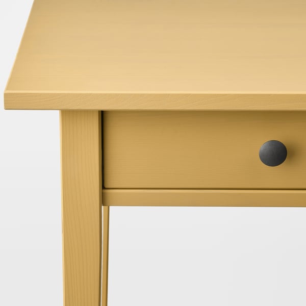 A close-up of a yellow wooden table with a smooth, sleek finish and a circular drawer handle.