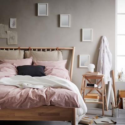 Cosy bedroom with wooden bed, pink pillows, mirrored headboard, side table with lamp, clock, and easel.