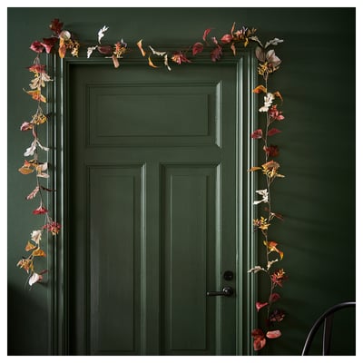 Autumn garland in reds, oranges, and browns, draped on a dark green door, indoors or out.