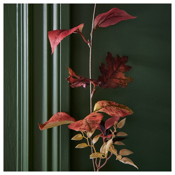 Artificial autumn leaves garland with reddish-brown hues displayed against a green wall, showcasing lifelike quality and vibrant colours.