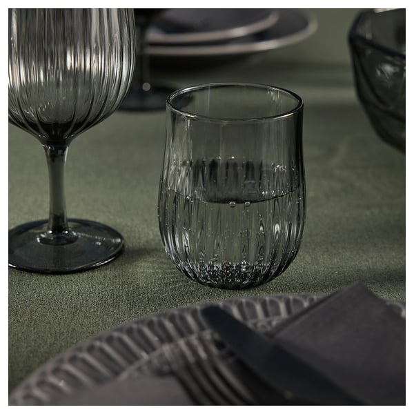 Two elegant, ridged glasses on a green tablecloth. One holds a small amount of water.