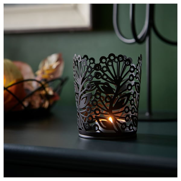 Dark green wall setting with a lit metal tealight holder, casting decorative shadows, part of the HÖSTAGILLE collection.