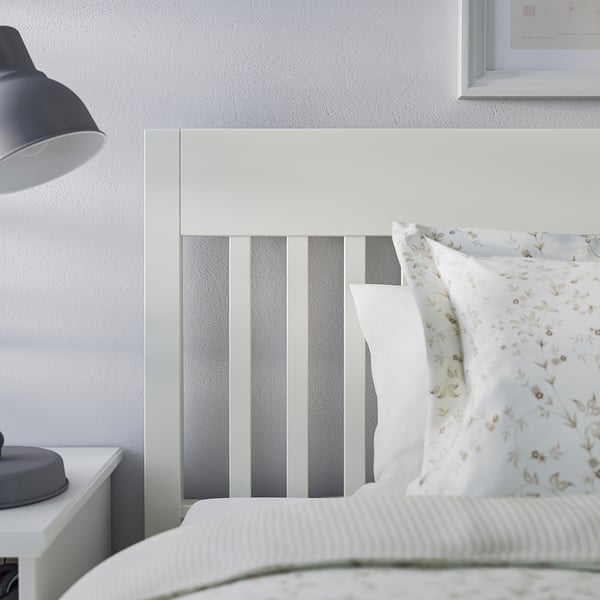 A white IDANÄS bed frame with a grey ombre headboard, a floral pillow, and a blue lamp.