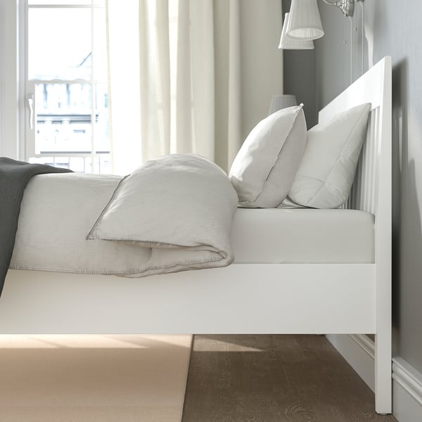 Bright, minimalist bedroom with white IDANÄS bed, crisp linens, soft lighting, and city view.