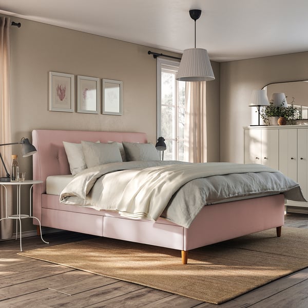 Modern bedroom with IDANÄS pink upholstered bed, white linens, grey rug, wooden floor, pendant lamp, and white cabinet.