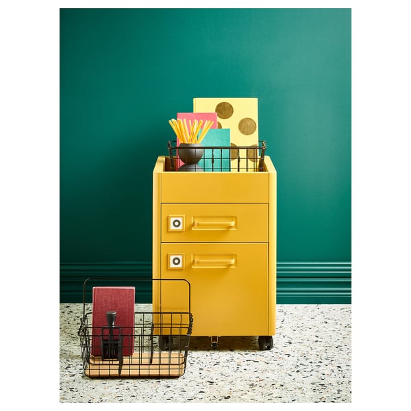 Yellow IDÅSEN filing cabinet with 3 drawers, colourful items, black mesh basket, teal wall.