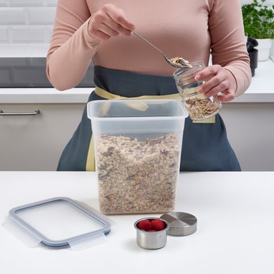 A person is scooping granola from a clear IKEA 365+ container on a kitchen counter, which has a snap-lock lid ensuring freshness and preventing leaks.