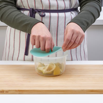 Person holding turquoise lid over IKEA jar filled with lemon slices on a wooden countertop.