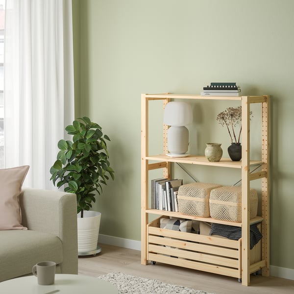 Light wooden IVAR shelving unit with various items, larger than couch and plant next to it.