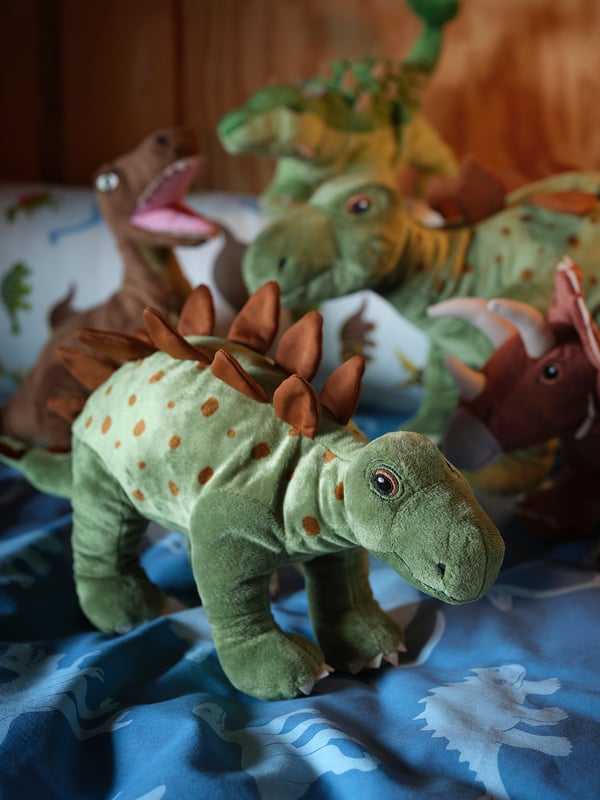 Toy dinosaurs, green with brown spots, soft fabric, playful shapes, on blue bedspread.