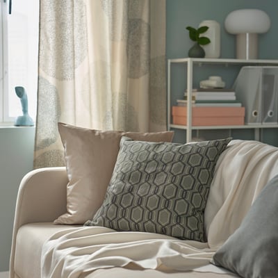 A cosy armchair with JÄTTEPOPPEL cushions in dark grey/white geometric pattern and a velvet taupe pillow.