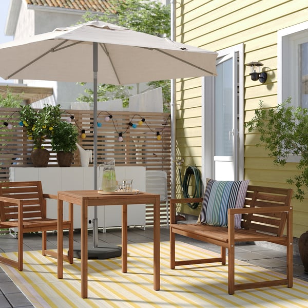 Outdoor patio with wooden table, four chairs, and large beige parasol offering shade on a yellow and white striped rug.