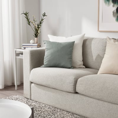 Living room with green, eco-friendly KÄRLEKSGRÄS cushion on light sofa.