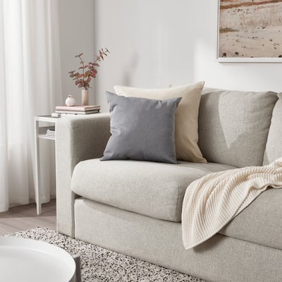 Modern living room with KÄRLEKSGRÄS cushion sofa, blanket, and side table with vase and books.