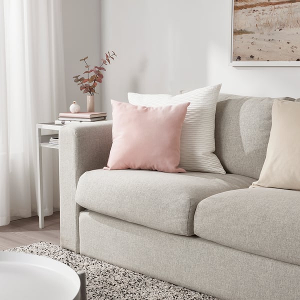 Cosy living room with grey sofa, light pink KÄRLEKSGRÄS cushion, white stripe pillows, decorative vase on side table, and artwork on wall.