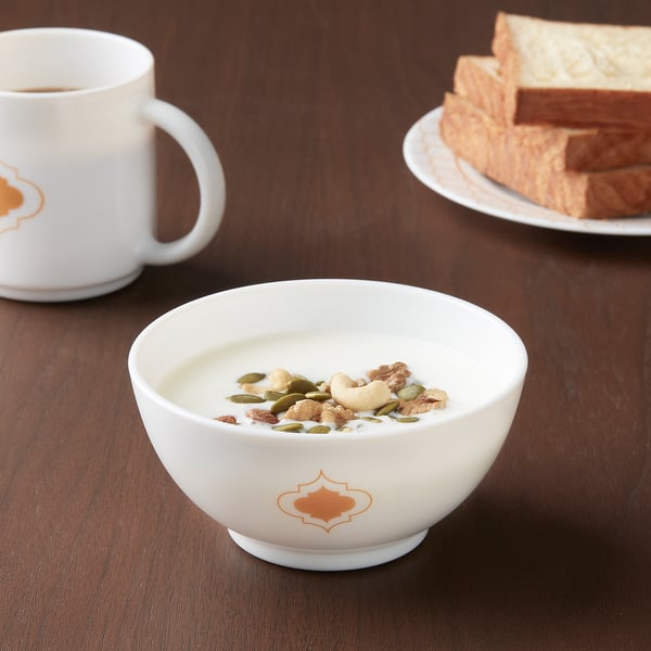 KALASBRA white bowl with orange design, made of tempered glass, smaller than mug and plate, filled with yoghurt and nuts.