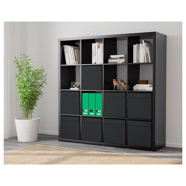 Black KALLAX shelving unit with mix of open and closed storage, holding books and decorative items, positioned against a wall.