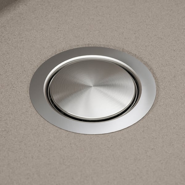 Silver circular drain cover set in a grey sink, reflecting light, indicating high-quality stainless steel and smooth surface.