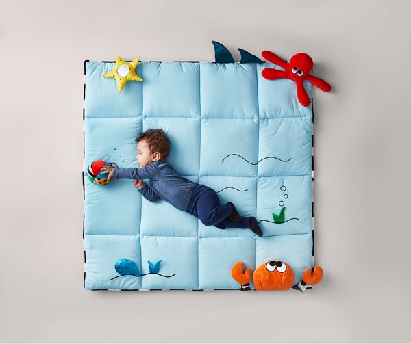 Baby on blue ocean-themed play mat with plush sea creature toys, including star, shark, crab, and octopus.