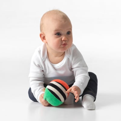 Baby sits playing with multicoloured ball, stimulating senses and discovery.