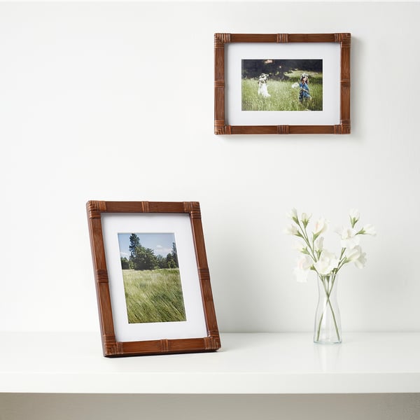 Two picture frames show grassy scenes; one stands, one hangs with a vase.