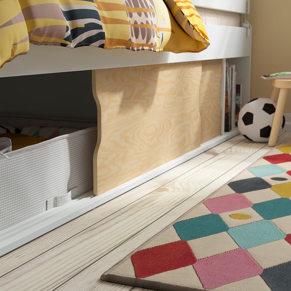Childs bed with colourful bedding, ensures safety with guardrails, sliding doors for storage. Bright, patterned rug on light-colored floor.