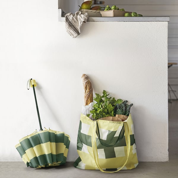 KNALLA bags: yellow, green tote with groceries, compact umbrella. Near fresh produce and cloth.