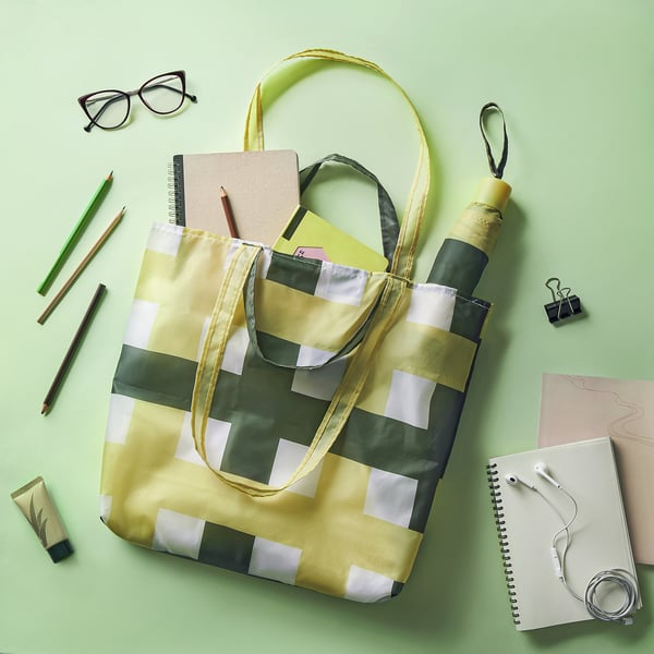 Yellow KNALLA tote bag with stripes, filled with supplies. Made of recycled polyester.