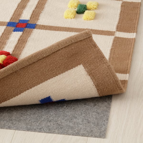Beige and brown patterned wool rug with colourful pom-poms and anti-slip felt pad underneath.