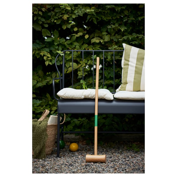 Black chair with KUDDARNA cushions, game set on pebbles, lush greenery.