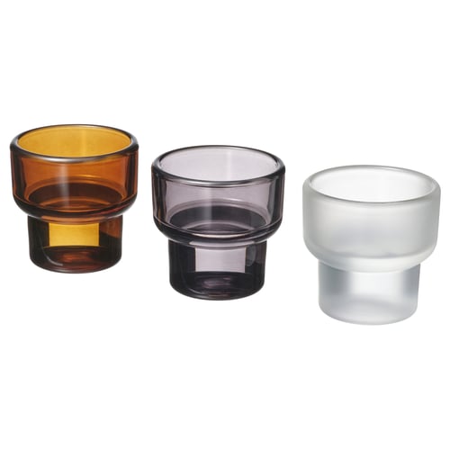 Three colourful, cylindrical glass tealight holders in brown, grey, and white are arranged side by side, showcasing their simple and elegant design.