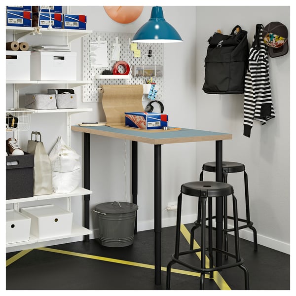 A modern, organised work corner with a black LAGKAPTEN desk, blue lamp, and pegboard storage.