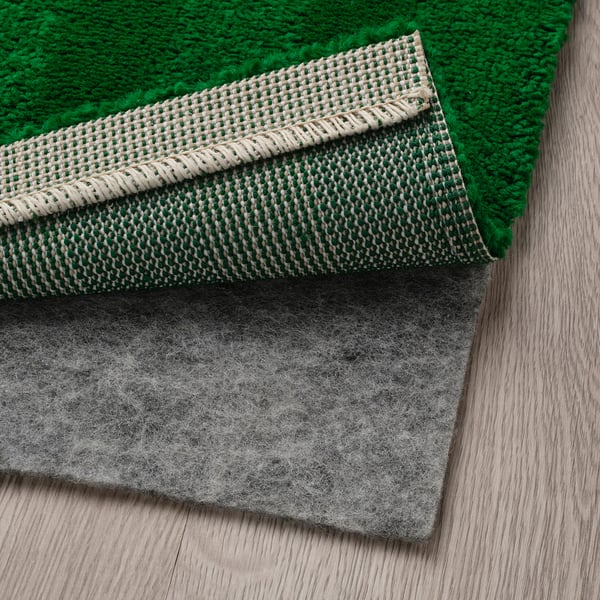 Green rug with curly yarn stripes, soft and great for bedrooms, shown with non-slip pad underneath.