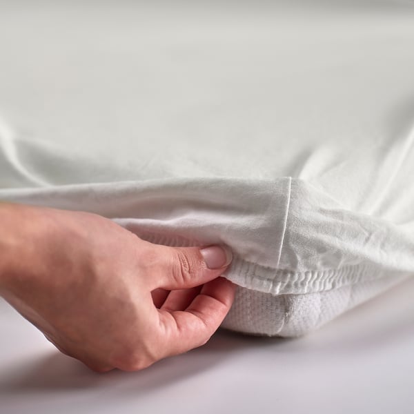 Hand tucking white LEN fitted sheet onto mattress.