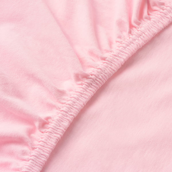 Close-up of soft pink cotton fitted sheet, showing smooth texture and sturdy elastic edge, indicating quality craftsmanship.