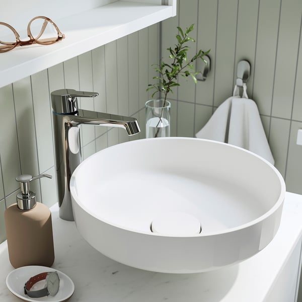 Modern bathroom sink with chrome tap, soap dispenser, small plant, and white storage lid.