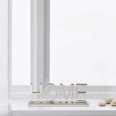 Silver home sign sitting on a white shelf near a window.