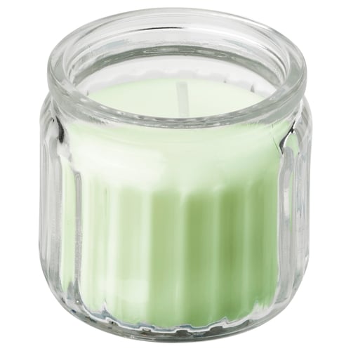 A small, clear glass candle jar with a green apple-scented candle inside. It is cylindrical with vertical ridges.