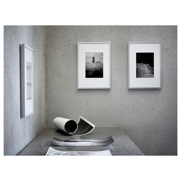 Three framed black & white photos hang on a grey wall. Below, a white cylinder lies on a black sculpture.