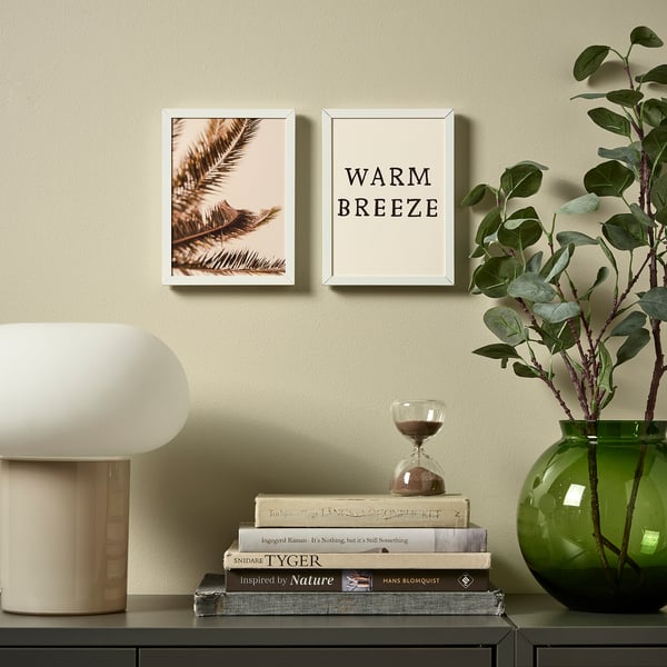 Wall art display with warm breeze poster, surrounded by decor including lamp, books, and plant. Frame adjustable for vertical or horizontal hanging.