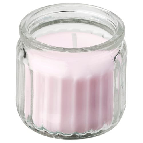 A LUGNARE scented candle in a clear glass jar with fluted sides. The candle is light pink and made from a combination of plant-based and paraffin wax.