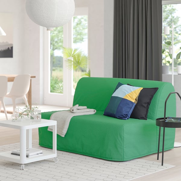 Modern living room with green lycksele sofa, natural light, colourful pillow, coffee table with plant, and black side table.