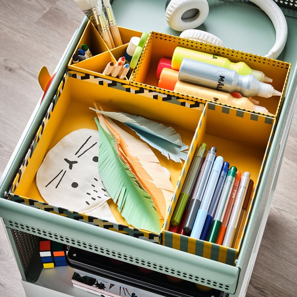 Organised kids craft supplies in colourful lysmak boxes. Yellow box divided with colourful markers, pens, glue, feathers, and paper.