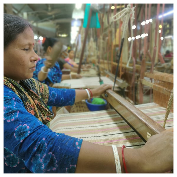 People weave fabric on traditional looms in workshop.