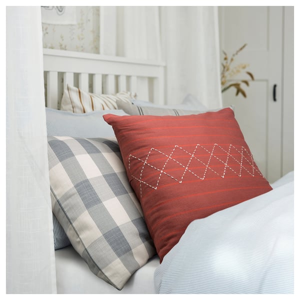 Bright red and plaid blue pillows on white bed, bold geometric pattern on red pillow.