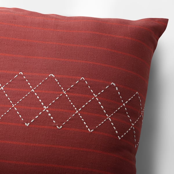 Close-up of red cushion cover with subtle stripes, featuring intricate white hand-embroidered geometric design.